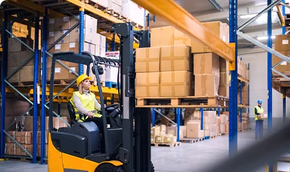 Worker operating yellow forklift in industrial warehouse with safety vest