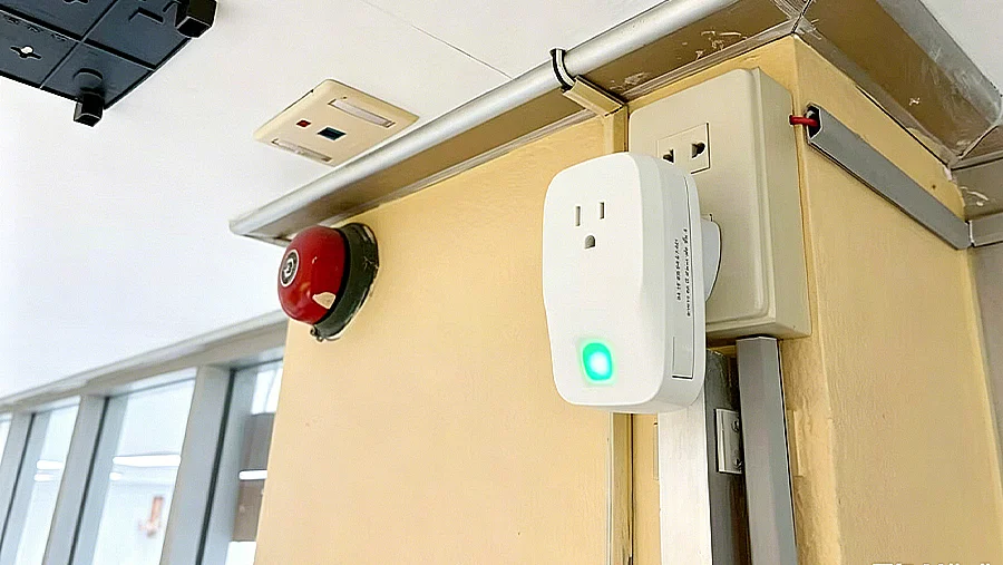 MK107 BLE plug gateway with green LED indicator installed in a hospital wall outlet next to a red fire alarm bell